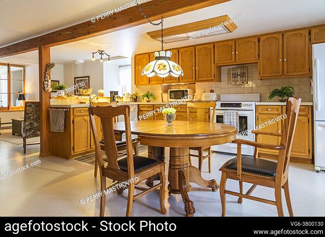 Red pine wood claw foot dining table with red oak wood and black leather seat high back chairs in kitchen with oak wood cabinets and white ivory linoleum...