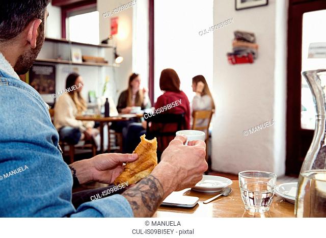 Man having breakfast, distracted by women on next table