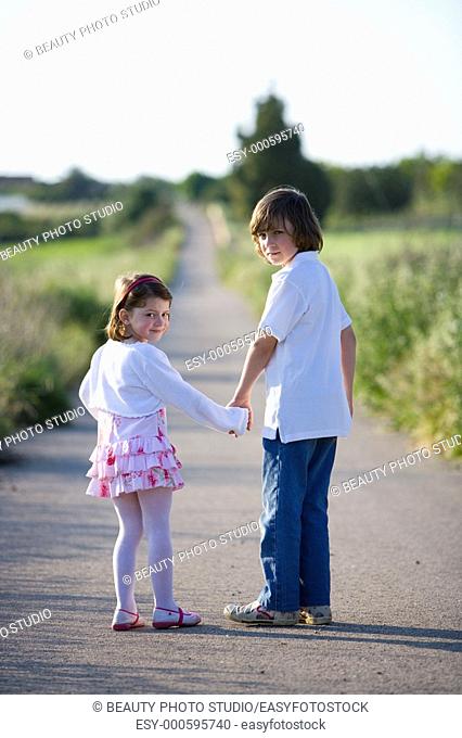 A boy and a girl hand in hand walking on a country road