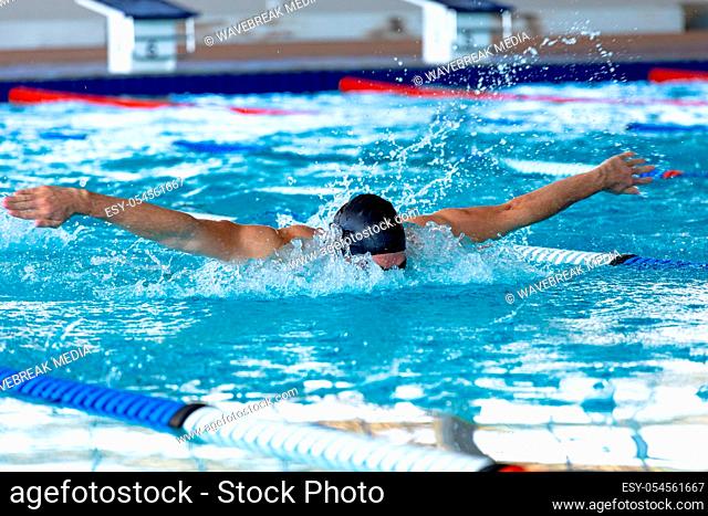 Front view of a male swimmer at swimming pool, wearing a black swimming cap splashing, swimming butterfly. Swimmers training hard for competition
