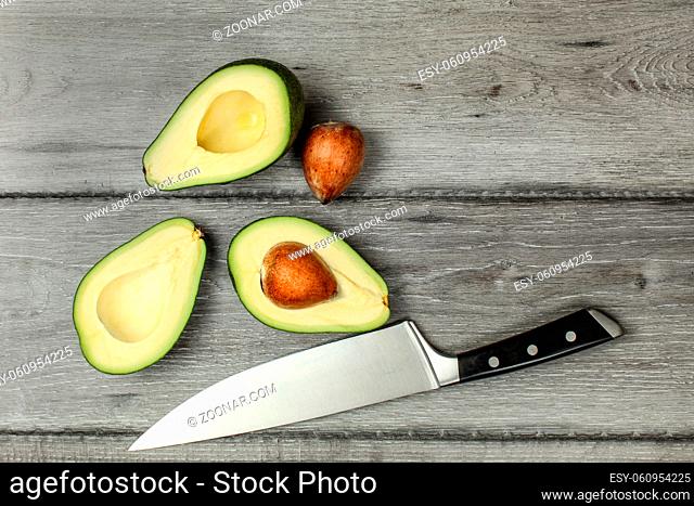 Tabletop view, two avocados cut in half, seeds visible, with chef's knife next to them