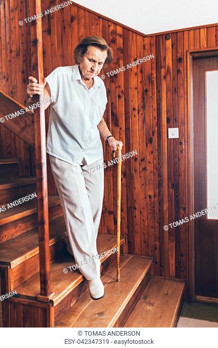 Elderly woman at home using a walking cane to get down the stairs