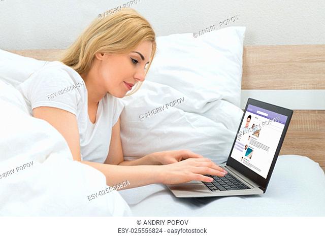 Young Woman In Bed With Laptop Chatting On Social Networking Site