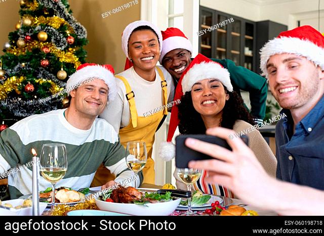 Group of happy diverse female and male friends in santa hats , celebrating christmas, taking selfie