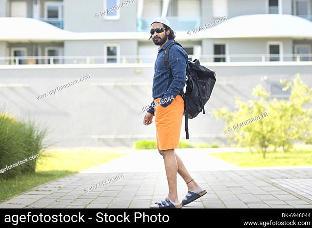Young man with bag, sunglasses, cap and shorts in the city, Freiburg, Baden-Württemberg, Germany, Europe