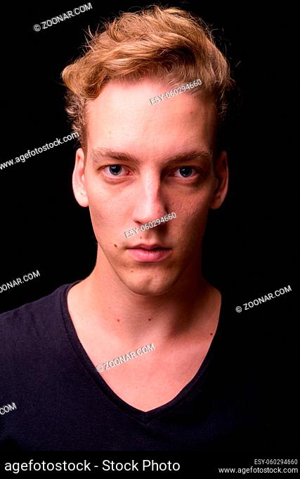 Studio shot of young handsome Scandinavian man with blond hair against black background