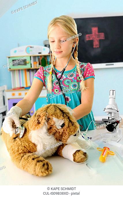 Girl pretending to be vet examining toy tiger using stethoscope