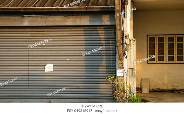 Dirty Vintage Roller Shutter Door with Blank Paper Note - Old Abandoned House for Sale in Bangkok Thailand. Sunny Warm Day