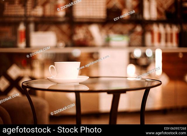 Hairdressing salon interior. Coffee cup on glass table and chair for client in beauty parlor with nobody, illuminated mirror in blurred background