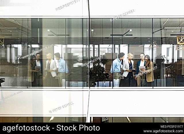 Businesswoman and empoyees talking behind windowpane in office