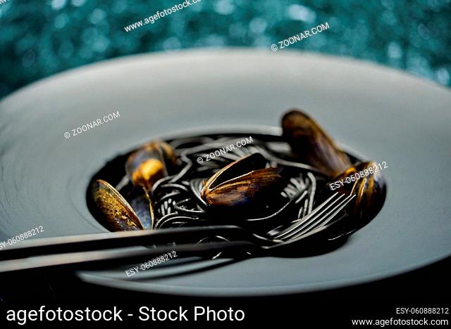 Seafood black spaghetti pasta with clams served on black plate on dark stone background. Side view, flat lay