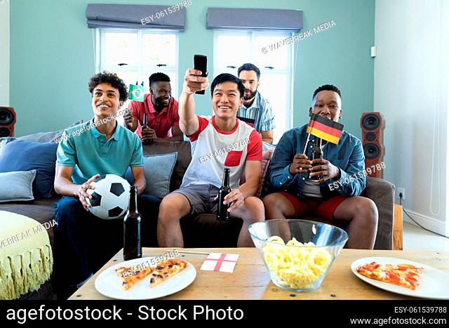 Multiracial male friends with beer bottles, flags and ball watching soccer match at home, copy space