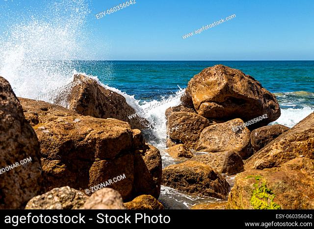 Splashes from a wave splashing on the rocks in sunny day