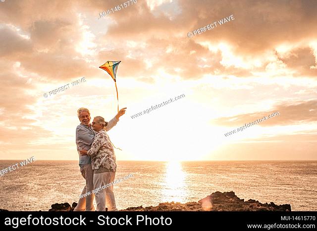 couple of two happy and fun senior or mature people enjoying and playing at the beach with their flying kite - summer lifestyle