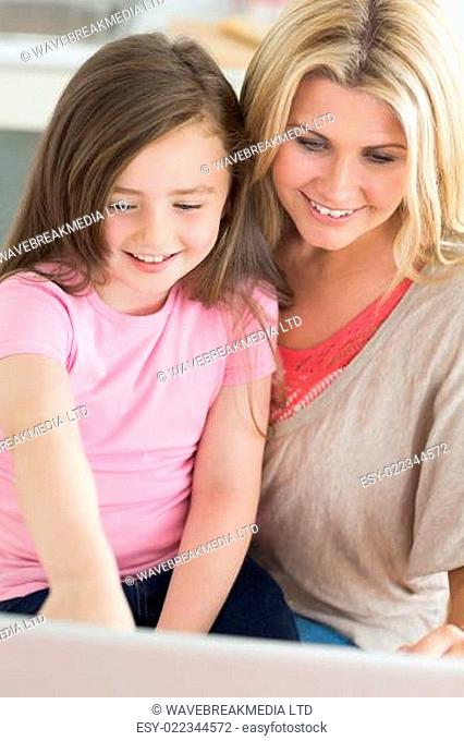 Mum and child sitting at the kitchen smiling at laptop