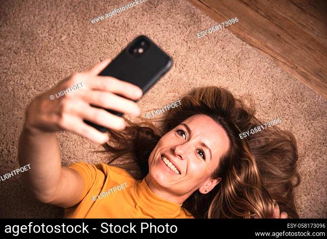 Happy mid-aged woman taking selfie with her smart phone at home