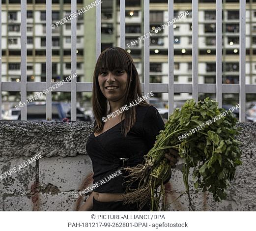 16 December 2018, Venezuela, Caracas: Maria Requena smiles as she holds two bundles of parsley in her hands at a market. At this market