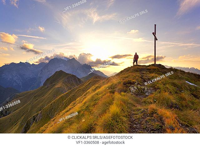 A hiker admires the sunset on Marmolada group from the grassy summit of Migogn Mount, Dolomites, Marmolada group, Rocca Pietore, Belluno province, Veneto, Italy