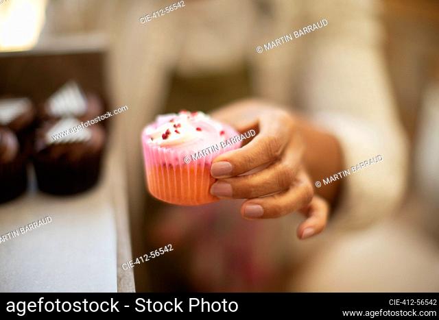 Close up female baker holding cupcake in pink liner