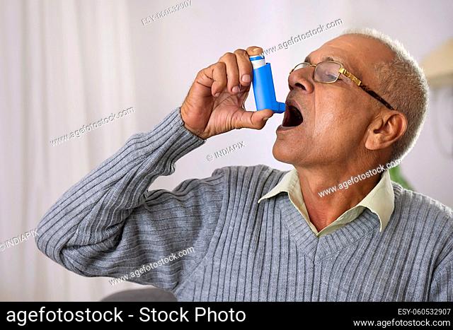 Old age man using her Asthma Inhaler at home
