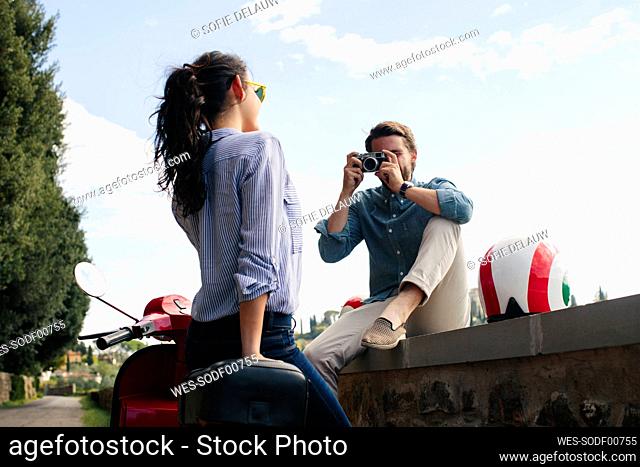 Man photographing girlfriend standing by Vespa