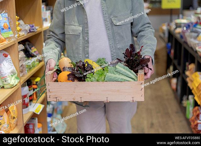 Close-up of senior man carrying crate with vegetables in a small food store