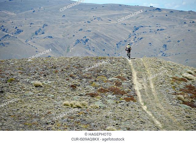 Woman cycling in remote landscape, New Zealand