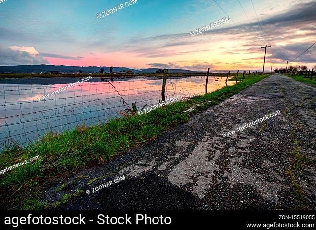 A flooded field along a country road at sunset