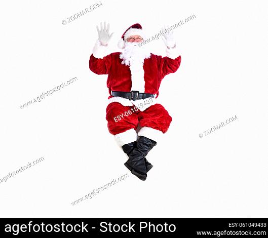 Senior man in traditional Santa Claus Suit sitting on a white wall with both hands in the air. Isolated on white with copy space