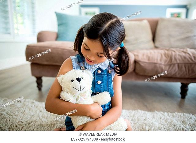 Smiling girl playing with teddy bear in living room