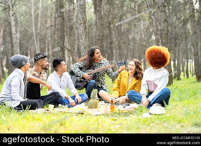 Young male and female friends playing guitar during picnic at forest