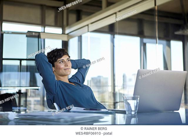 Smiling businesswoman sitting at desk in office with laptop having a break