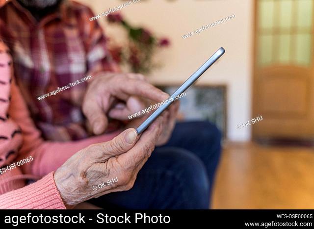 Mature man teaching tablet PC to senior woman in living room