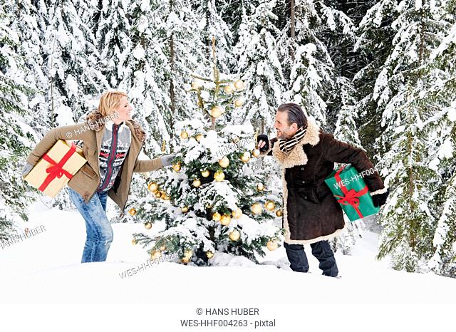 Austria, Salzburg County, Couple holding christmas gift in snow, smiling