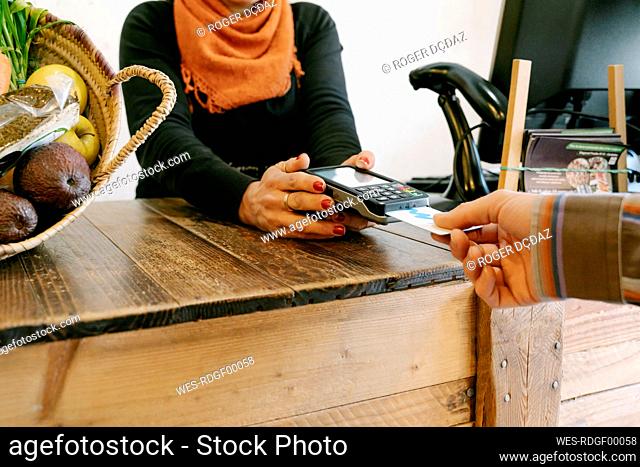 Female cashier assisting customer in payment through credit card at checkout in store