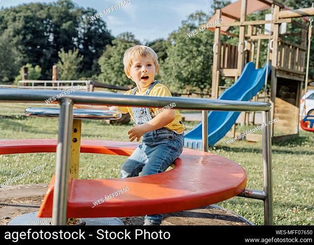 Charming boy sitting on merry go round in playground