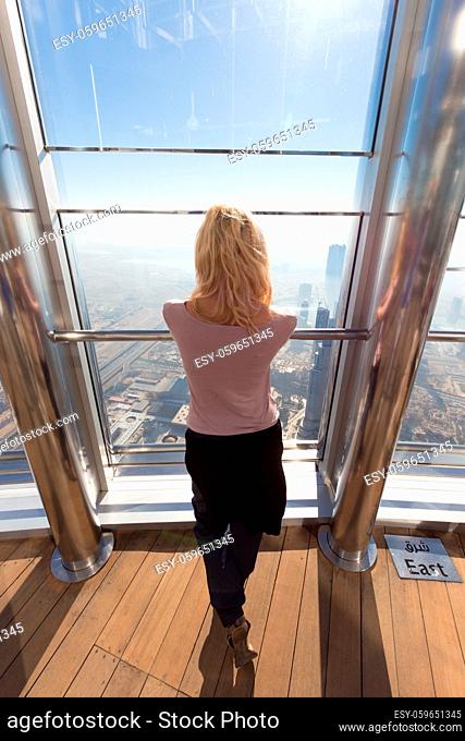 Beautiful lady admiring the city view from modern observing platform at the top of the tallest skyscraper in the world, Burj Khalifa in Dubai