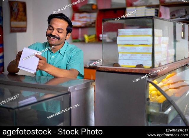 Portrait of happy Sweet shop owner maintaining accounts at counter