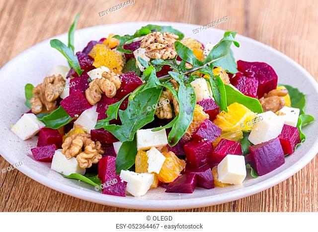 Healthy vegetarian salad with beetroot, green arugula, orange, feta cheese and walnuts on white plate, close up