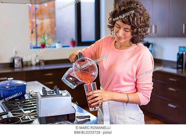 Hispanic woman pouring smoothie from blender into glassware