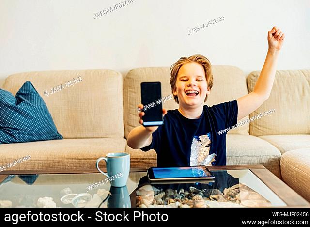 Happy boy in living room at home showing smartphone