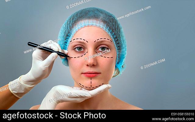 Front view of a plastic surgeon drawing lines on a face of young woman prior to cosmetic surgery. Concept of visage improvement and beauty healthcare in clinic