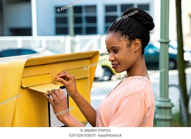 Young African Woman Inserting Letter In Mailbox