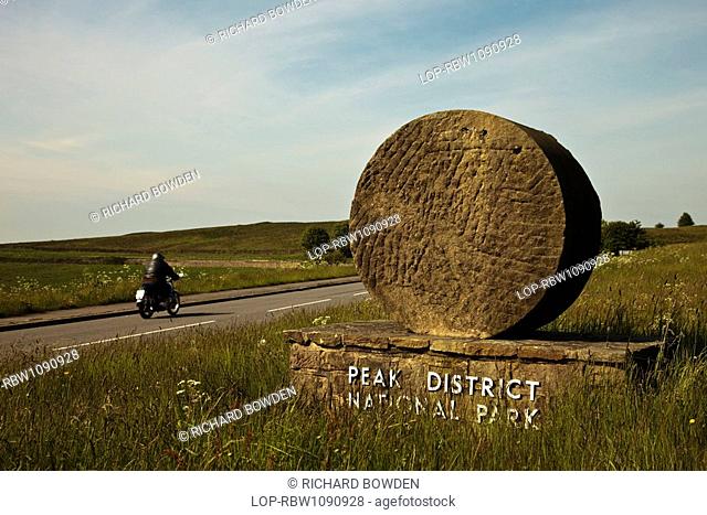 England, Derbyshire, Curbar, A lone motorcyclist rides into the Peak District National Park past one of the stone signs that marks Britain's first national park
