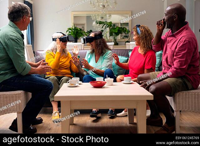 Happy multiracial senior woman and men with friends using vr headsets in living room at home
