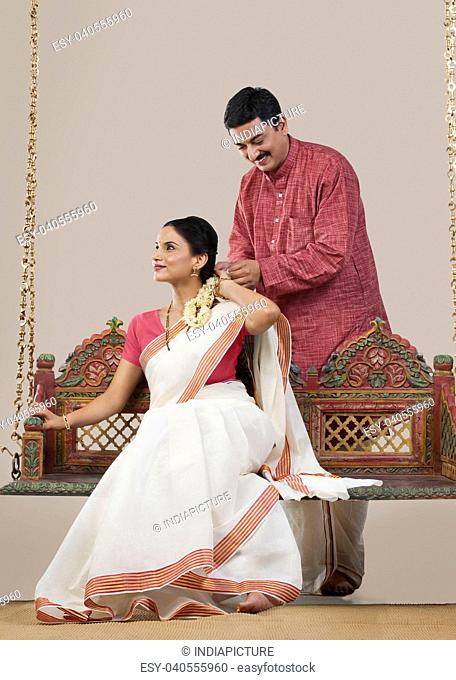 South Indian man tying a Gajra on his wife's hair