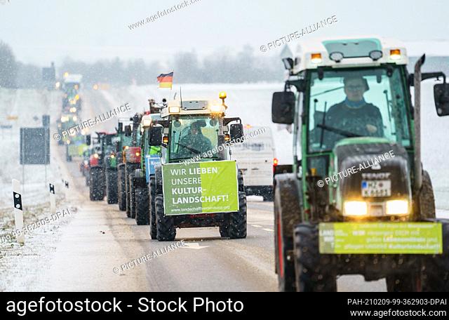 09 February 2021, Rhineland-Palatinate, Alzey: The tractor protest procession is driving on a country road towards Alzey with a protest poster with the...