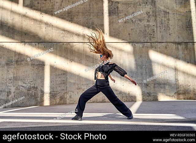 Woman with hair toss dancing on street in front of wall