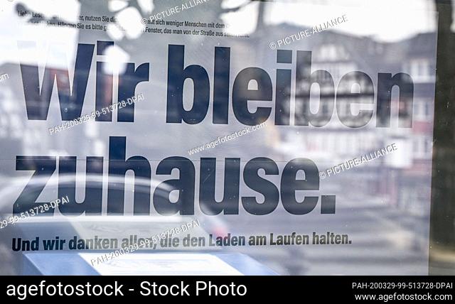 29 March 2020, Hessen, Biedenkopf: ""How to stay at home"" is written on a screen in the shop window of the office of a local newspaper