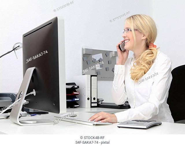 Smiling young woman in office on the phone